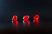 Drei rote, leuchtende Granatapfelkerne vor dunklem Hintergrund