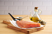 Raw salmon fillet placed on cutting wooden board near spoons with salt and pepper on wooden table