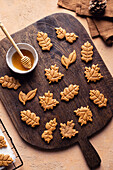 Leaf shaped sweet baked cookies placed on wooden cutting board near bowl of honey in kitchen