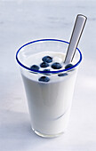 A glass of yogurt with some blueberries and spoon