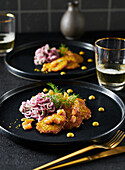 Mini salmon cakes with onion salad on a black plate, with golden cutlery