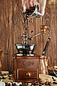 Pouring aromatic coffee grains in vintage mill placed on wooden table