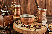 Metal cup of aromatic drink placed on wooden table with vintage coffee grinder and cezve
