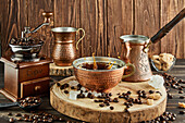 Metal cup of aromatic drink placed on wooden table with vintage coffee grinder and cezve