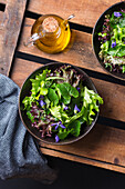 Vegetarian salad with green and red lettuce leaves and edible flowers against jug of oil