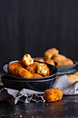 Tasty croquettes with cheese filling and golden crust in bowl on towel on dark background
