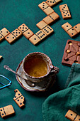 Sweet domino shaped cookies placed on green background with cup of hot drink and chocolate pastry