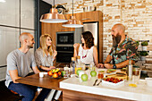 Men and women chatting with each other while gathering around table and having healthy breakfast in loft kitchen at home
