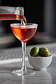 Chilled Negroni being poured into an elegant glass served with olives on a bar