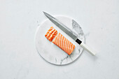 Rohes Lachsfilet mit einem japanischen Messer auf Marmorbrett