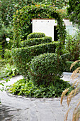Gartenweg in gepflegtem Garten mit Buchsbaumfiguren und grüner Laubenpforte