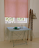 Organza cloth on table with crockery at window with closed pink roller blind