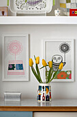 Yellow tulips in vase on sideboard with artwork