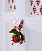 Berries in gingham ribbon tied around glass door handle of white painted wardrobe