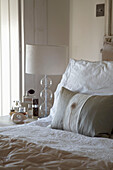 Lampshade and perfume bottles on bedside table with pillows and duvet