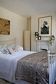 Seidensteppdecke auf dem Bett mit Kunstwerken in einem Zimmer mit originalem Kamin