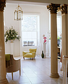 A modern living room decorated in a classical style plinth displaying flowers next to a green armchair tiled floor with stone columns in the foreground