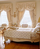 A traditional bedroom with a wooden floor an ornate antique double bed window with swag curtains armchair