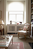 Glass-topped coffee table and chair at sunlit window of Arundel study, West Sussex