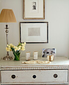 Lamp and flower arrangement on painted chest of drawers with distressed finish