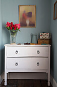 Red tulips in glass vase on white chest of drawers