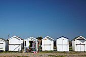 Woman stands outside beach hut in West Sussex, UK