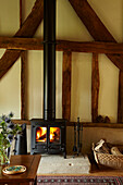 Lit wood burning stove and log basket in West Sussex home, England, UK
