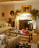 A traditional sitting room with period stone fireplace decorated for Christmas upholstered sofas wooden coffee table lit candles flower arrangements 