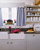 Landhausküche mit Doppelspüle, Granitarbeitsplatte, blauen Vorhänge am Fenster und Küchenregal mit Geschirr und Vorratsdosen