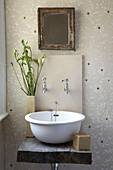 Flower arrangement next to washbasin on wooden shelf