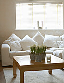 A detail of traditional country style living room with large corner sofa and low wooden table with flowers in baskets