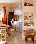 A country style open plan kitchen with dining area wooden panelling wood table bench seat wooden floor shelving hamper