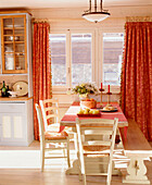 Offene Küche im Landhausstil mit Essecke, Holztisch, Stühlen, Sitzbank, Holzboden und roten Vorhängen