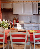 A country style open plan kitchen with dining area wood table chairs with rush seats painted cupboards table runners