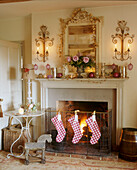 A detail of a traditional sitting room period fireplace decorated for Christmas stockings hanging from fireguard lit fire ornate mirror wall lights 