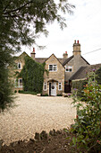 An exterior of a country house with gravel drive shrubs and trees front door open