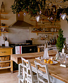 A traditional kitchen with decorations suspended above a large wooden kitchen table and an extractor fan above an stove