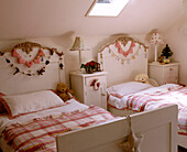 A traditional child's bedroom with a skylight in a sloped roof above seasonal decorations on the head boards and bedside tables