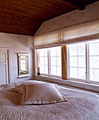 Doppelbett mit Steppdecke vor einem Fenster mit Raffrollos