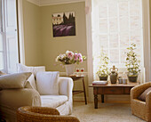 A traditional sitting room with a white sofa next to a several potted plants on a small wooden table in front of a window