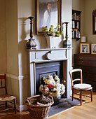 A traditional sitting room fireplace with a large display of flowers in a basket and an antique oil painting above the mantelpiece