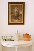 Gerahmtes Bild mit religiösem Motiv über einem kleinen, halbrunden Wandtisch mit Kerzenhalter und zwei Tongefäßen