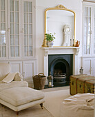 A traditional sitting room with a gold framed mirror above an open fireplace with a old wooden chest sitting in front