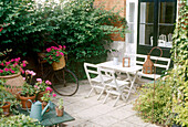 Terrassenbereich mit weißem Gartentisch und Stühlen daneben Fahrrad mit Blumenschmuck und ein kleiner Blumentisch