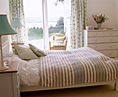 Double bed with stripe bed linen next to chest of drawers