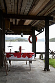 Tisch und Sitzbänke auf einer überdachten Terrasse mit Blick auf einen See