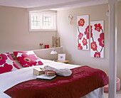 Double bed with red cover and pink floral patterned pillows with coordinated artwork