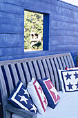 Wooden bench and cushions in front of blue painted timber wall