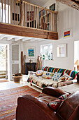 Gestreiftes Sofa mit Kissen und Vintage-Ledersessel in einem Haus mit doppelter Raumhöhe in Bridport, Dorset, Großbritannien
