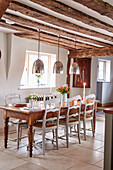 Silver pendant shades above wooden dining table with restored antique chairs in Grade II listed timber framed farmhouse Kent, UK